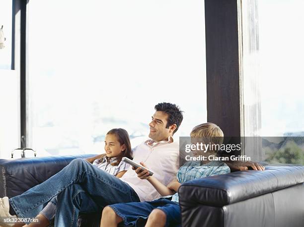 father watching television with his son and daughter - command sisters photos et images de collection