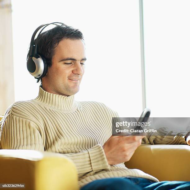 mid adult man wearing headphones and using a mobile phone - square neckline fotografías e imágenes de stock