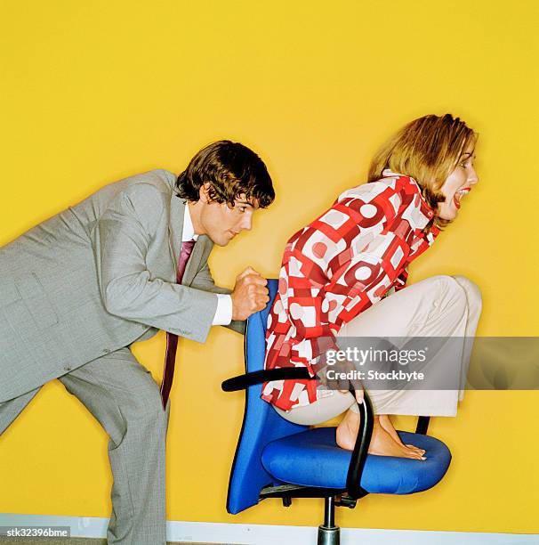 view of a young man pushing a young woman on a swivel chair - cadeira de escritório imagens e fotografias de stock
