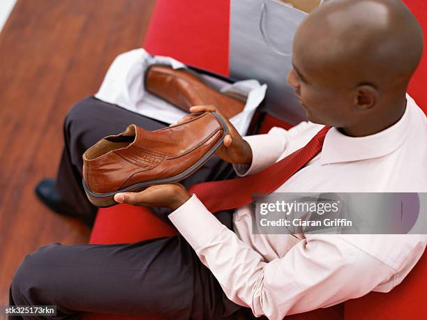 high angle view of a young man sitting on a couch holding a shoe - adrienne bailon and gillette ask miami couples to kiss tell if they prefer stubble or smooth shaven stock pictures, royalty-free photos & images