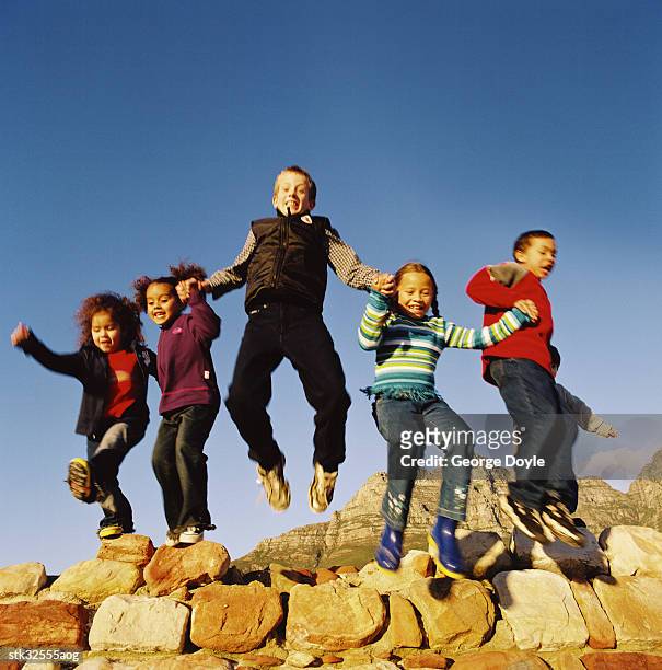 low angle view of a group of children holding hands and jumping off a rock - brian may signs copies of we will rock you at virigin megastore september 28 2004 stockfoto's en -beelden