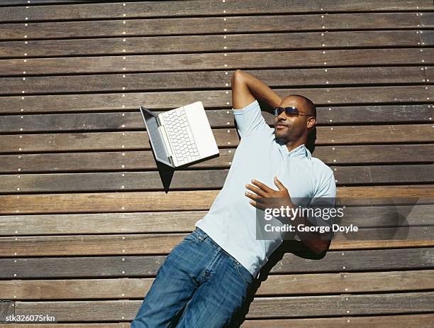 high angle view of a mid adult man lying on wooden planks with a laptop beside him - keri hilson and gillette ask los angeles couples to kiss tell if they prefer stubble or smooth shaven stock pictures, royalty-free photos & images