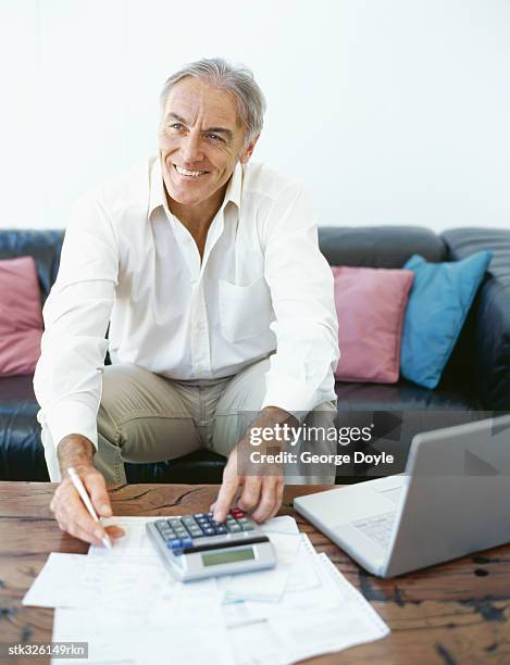 mature man doing paperwork with a laptop in front of him - writing instrument stock pictures, royalty-free photos & images