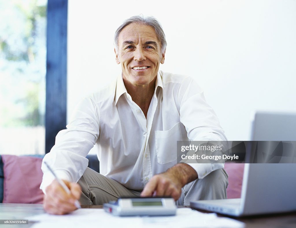 Mature man doing paperwork with a laptop in front of him