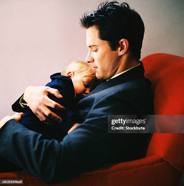 a young man sitting and holding his daughter in his arms - genderblend stock-fotos und bilder