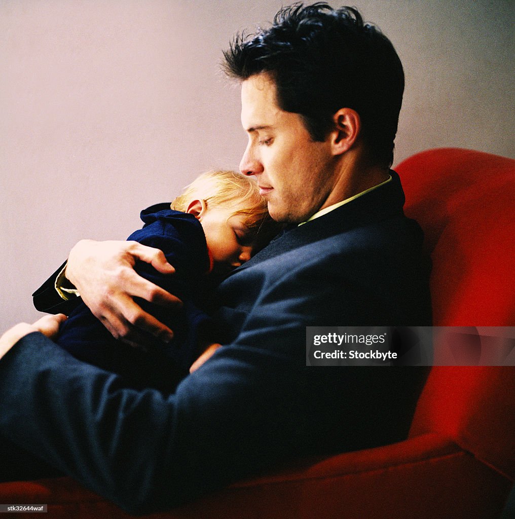 A young man sitting and holding his daughter in his arms