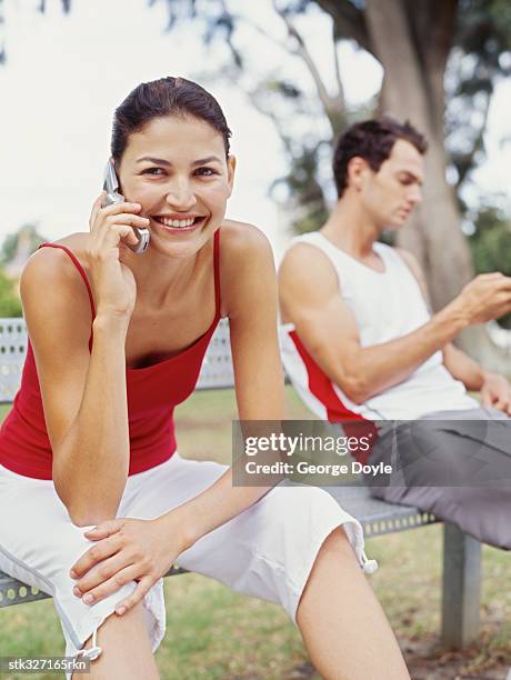 young woman talking on a mobile phone in a park - hand on knee stock pictures, royalty-free photos & images