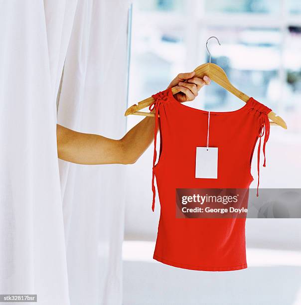 view of a woman standing in the changing room holding out a red top on a hanger - retail of amorepacific corp brands as south koreas biggest cosmetics makers revamps product lineup stockfoto's en -beelden