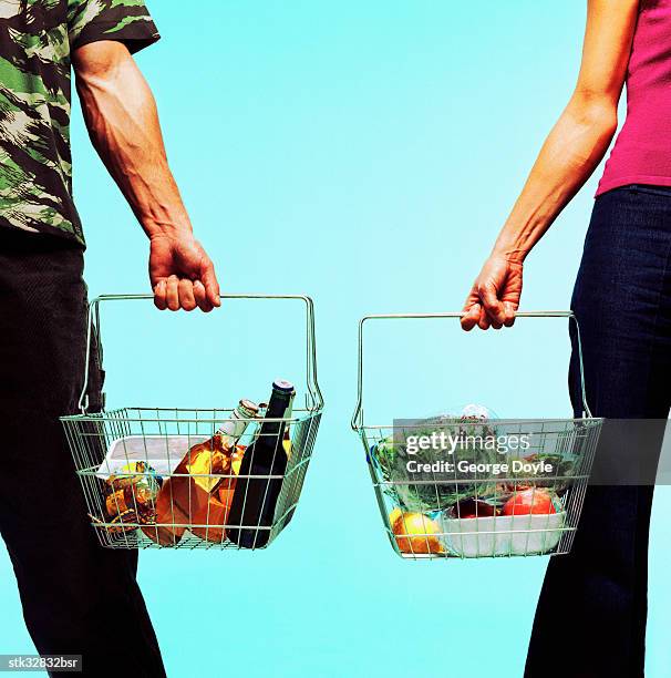 view of a man and a woman standing with goods in shopping baskets - cross entwicklung stock-fotos und bilder