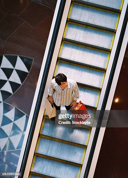 high angle view of a young man standing on an escalator with shopping bags - retail of amorepacific corp brands as south koreas biggest cosmetics makers revamps product lineup stockfoto's en -beelden