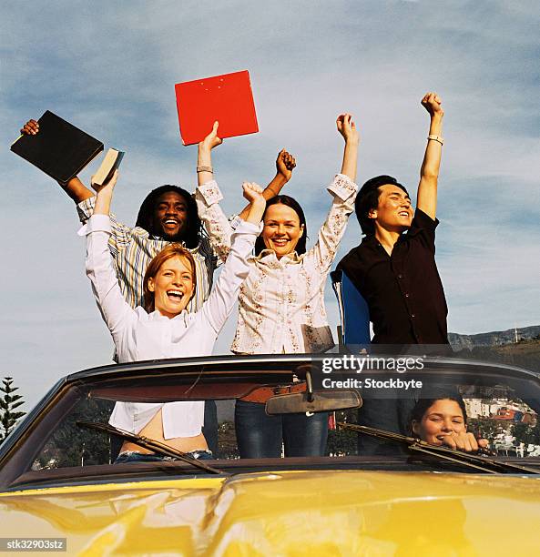 low angle view of a group of young men and women standing in a convertible car with arms raised in celebration - celebration imagens e fotografias de stock