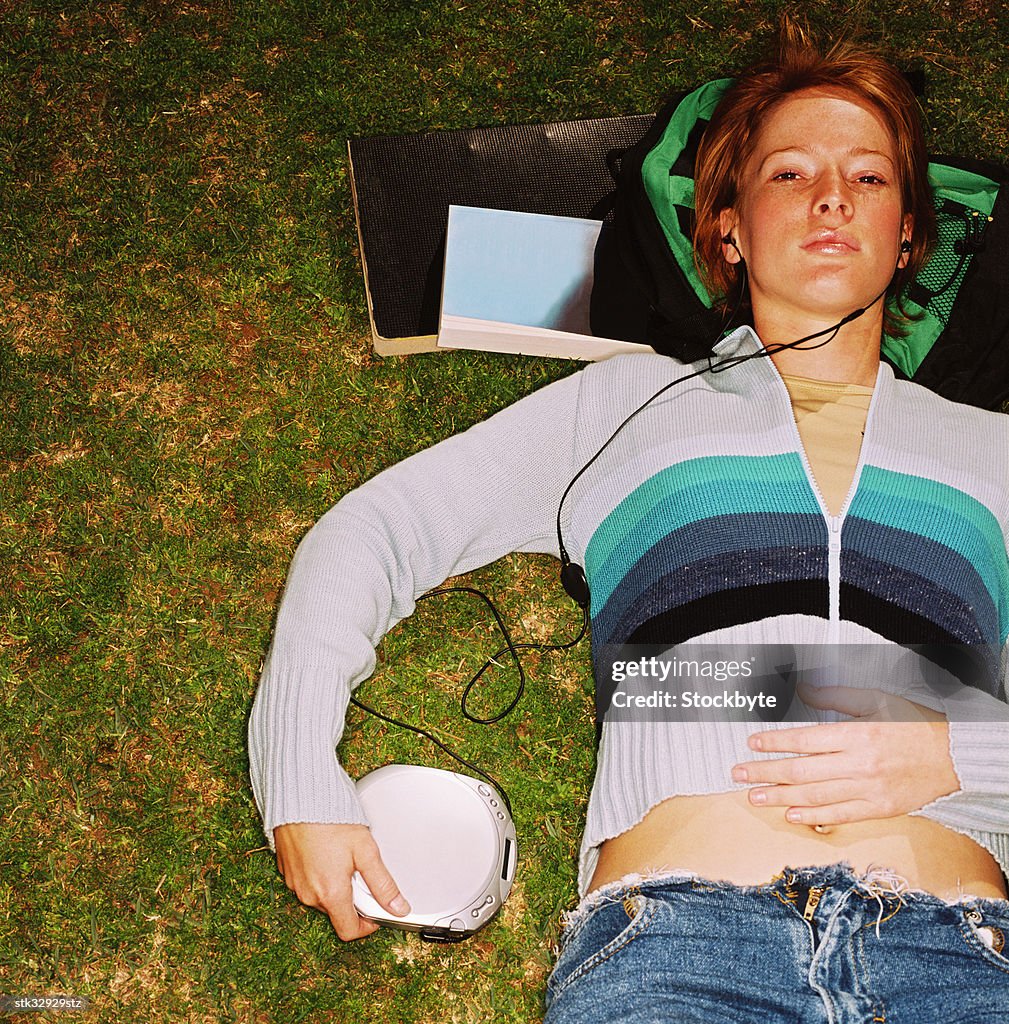 High angle view of a young woman lying on grass and listening to music through headphones