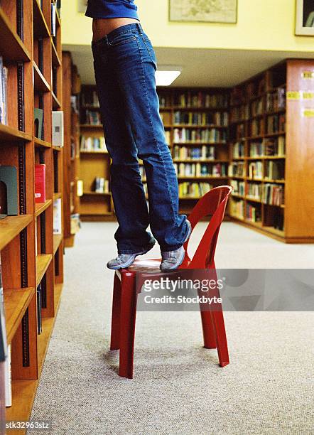 view of a person standing on a chair and reaching for a book - university of california students protest 32 percent fee hike stockfoto's en -beelden