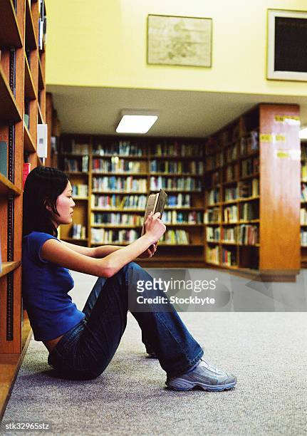 view of a young woman sitting on the floor and reading a book in a library - university of california students protest 32 percent fee hike stockfoto's en -beelden