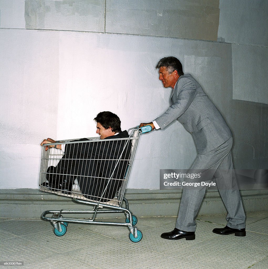 Side profile of a businessman pushing a man in a shopping cart