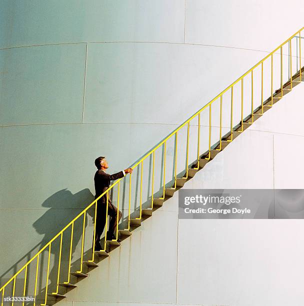 side profile of a man climbing the ladder of an industrial silo - cross entwicklung stock-fotos und bilder