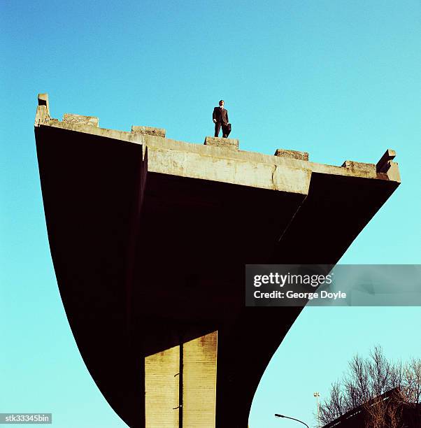 low angle view of a businessman standing atop an incomplete bridge - cross entwicklung stock-fotos und bilder