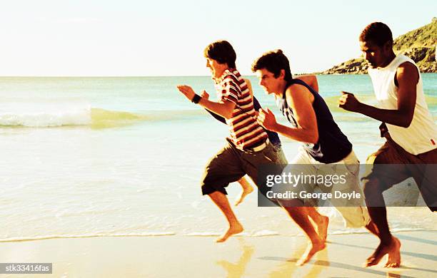 three teenage boys racing each other on the beach - other stock-fotos und bilder