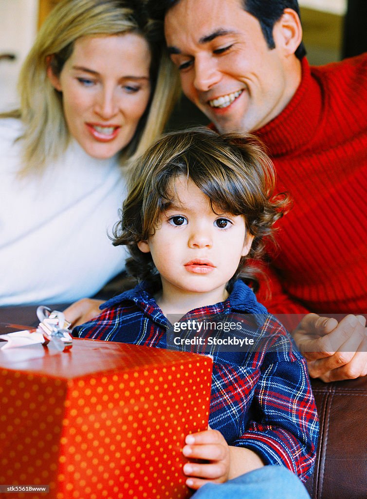 Portrait of a boy (4-6 years) holding a present with his parents behind him