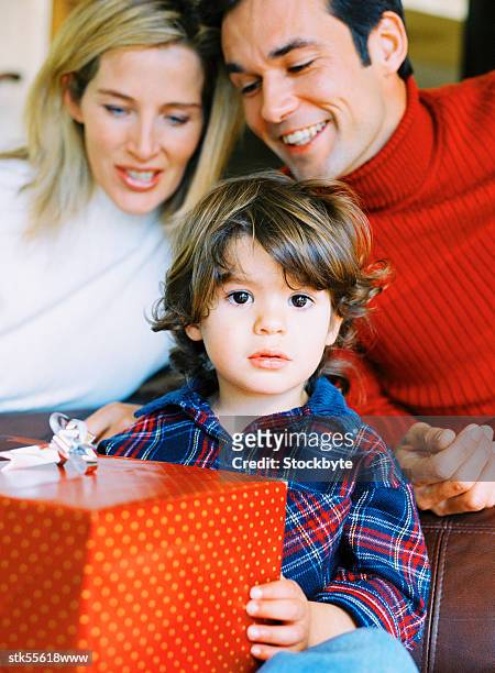 portrait of a boy (4-6 years) holding a present with his parents behind him - 30 34 years stock pictures, royalty-free photos & images