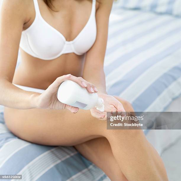 woman sitting at edge of bed pouring out lotion on to hands - get out stock pictures, royalty-free photos & images