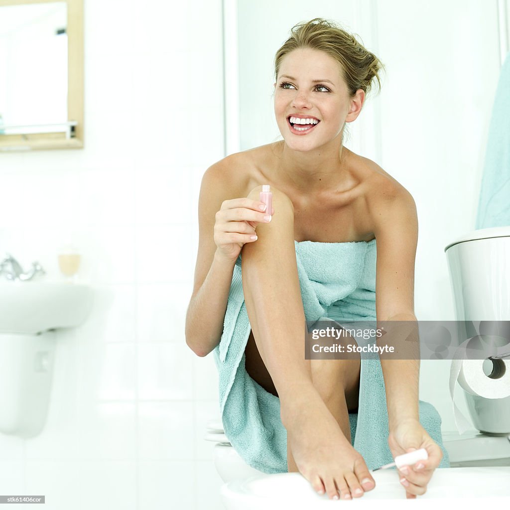 Portrait of a young woman in a towel painting her toenails