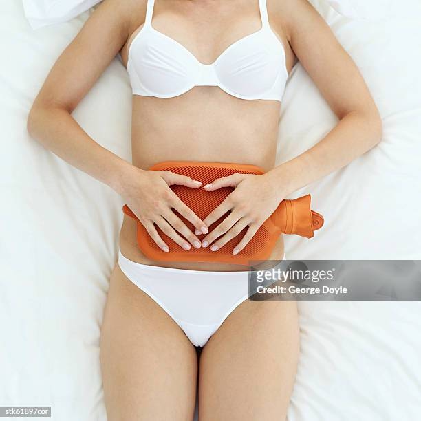 elevated view of a woman holding a hot water bottle on her stomach - wärmflasche stock-fotos und bilder