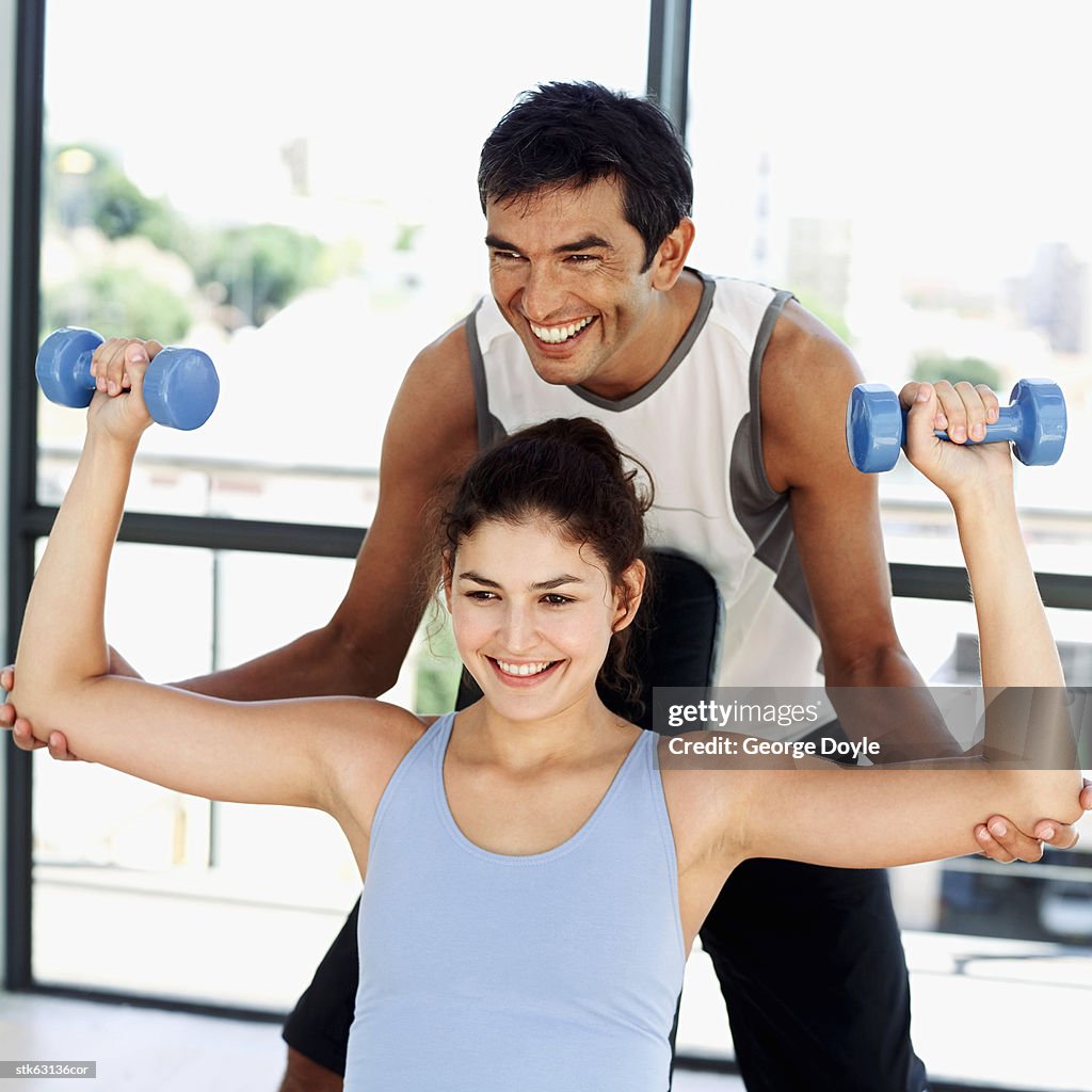 Close-up of a man helping a woman exercise using dumbbells