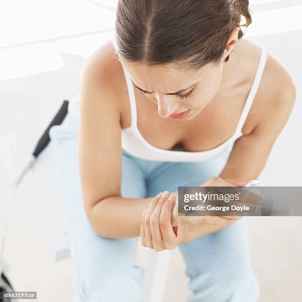 high angle view of a young woman sitting on a bench and holding her wrist - menschliches gelenk stock-fotos und bilder