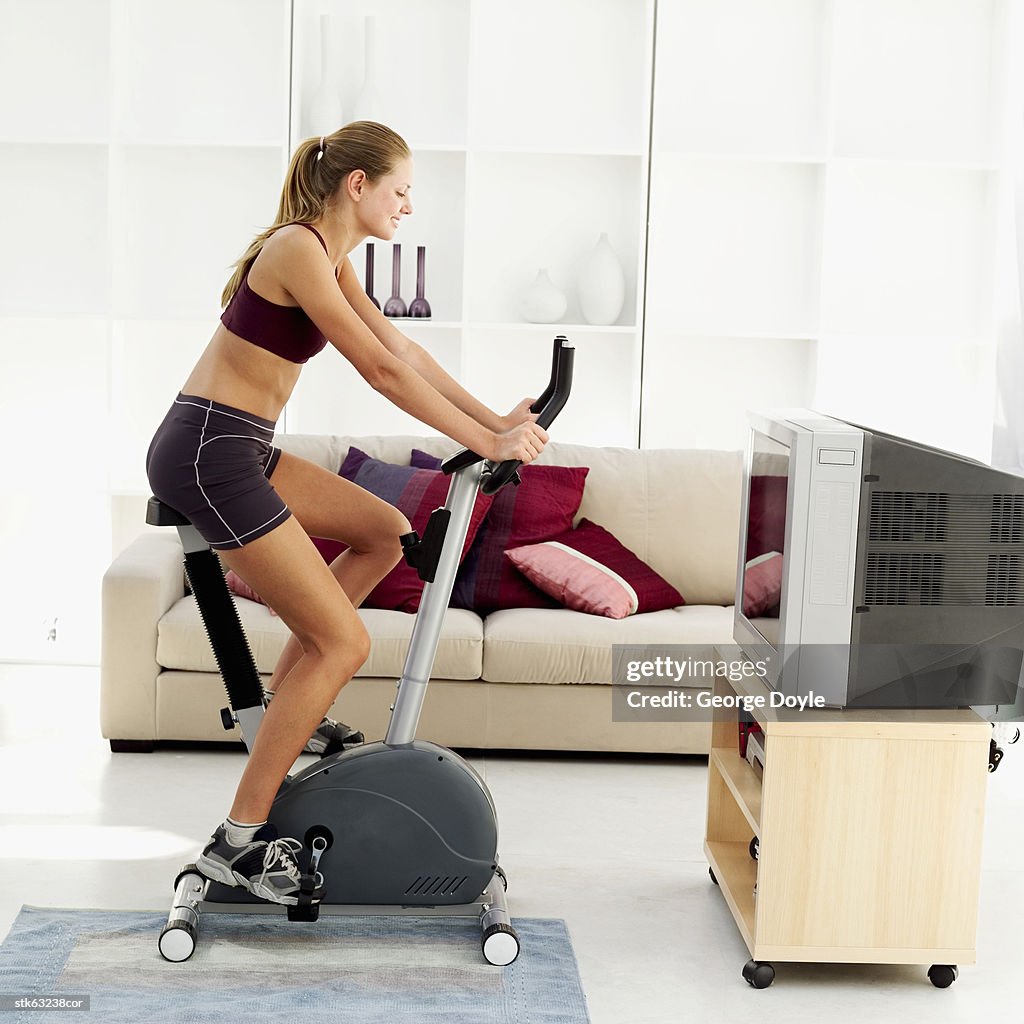 Side view of a woman exercising on an exercise bicycle in her living room