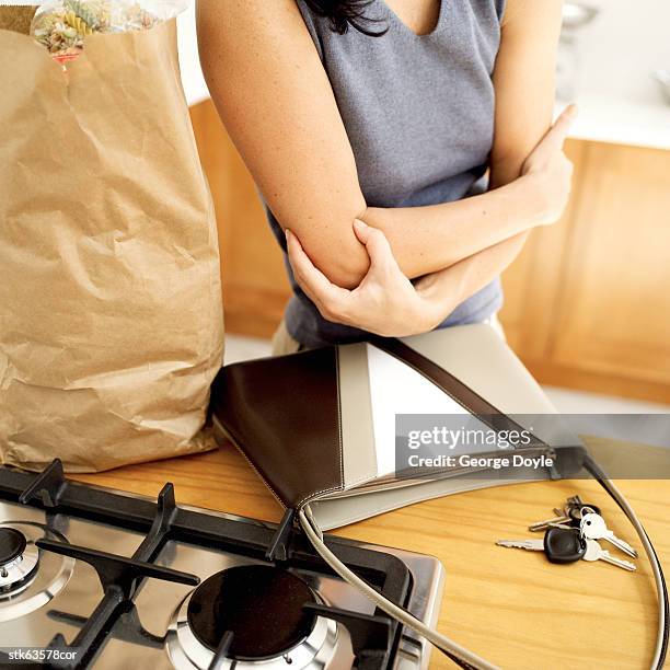 woman standing in front of the kitchen countertop grasping at her elbows - menschliches gelenk stock-fotos und bilder