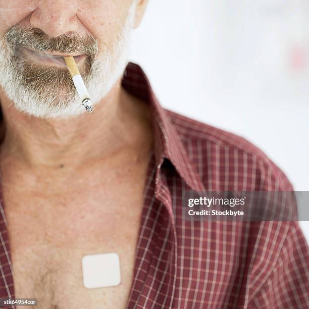 close-up of a man smoking cigarette and wearing a nicotine patch on chest - wearing stock-fotos und bilder