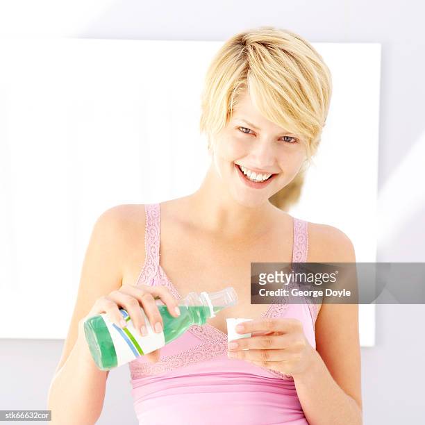 portrait of a woman taking mouthwash in a cup - mouthwash stock-fotos und bilder