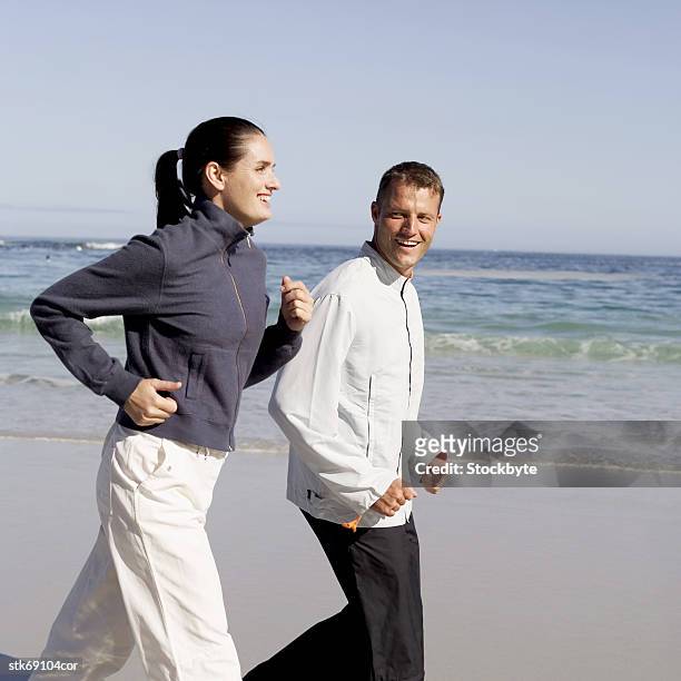 side profile of a couple jogging on the beach - in profile stock pictures, royalty-free photos & images