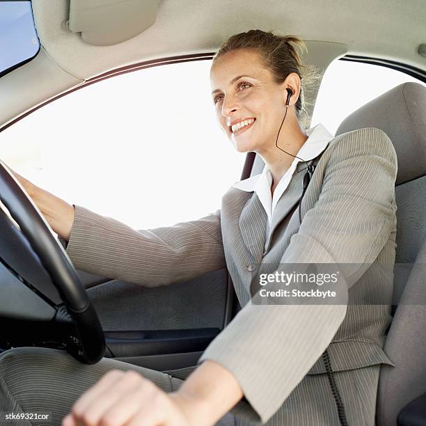 low angle view of a woman driving a car and wearing earphones - wearing stock-fotos und bilder