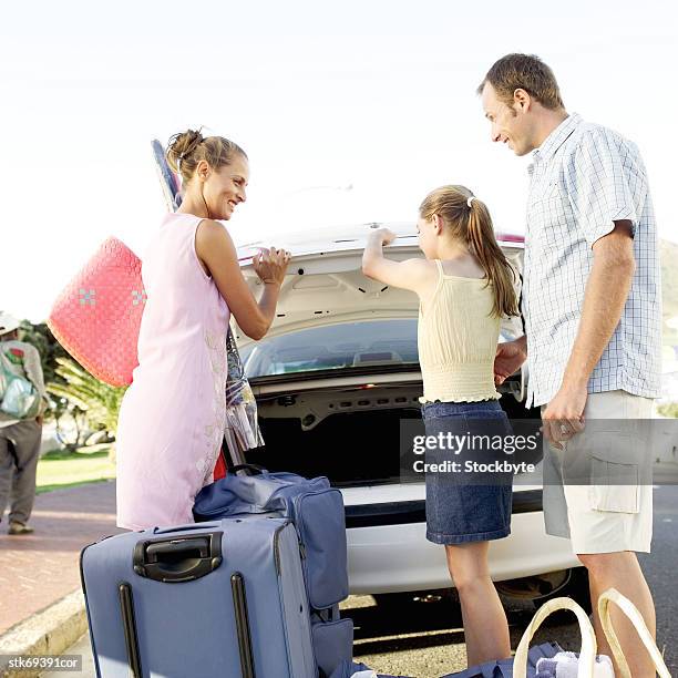 view from behind of parents unloading luggage with their daughter - closing car boot fotografías e imágenes de stock