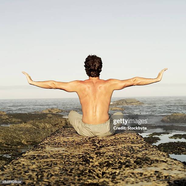 rear view of a man sitting on a rock at the beach doing yoga - brian may signs copies of we will rock you at virigin megastore september 28 2004 stockfoto's en -beelden