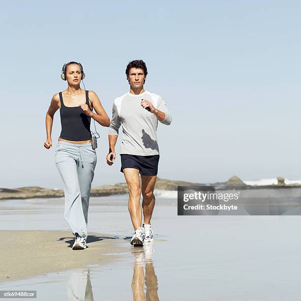 a woman wearing headphones and man holding handgrips while walking on the beach - wearing stock-fotos und bilder