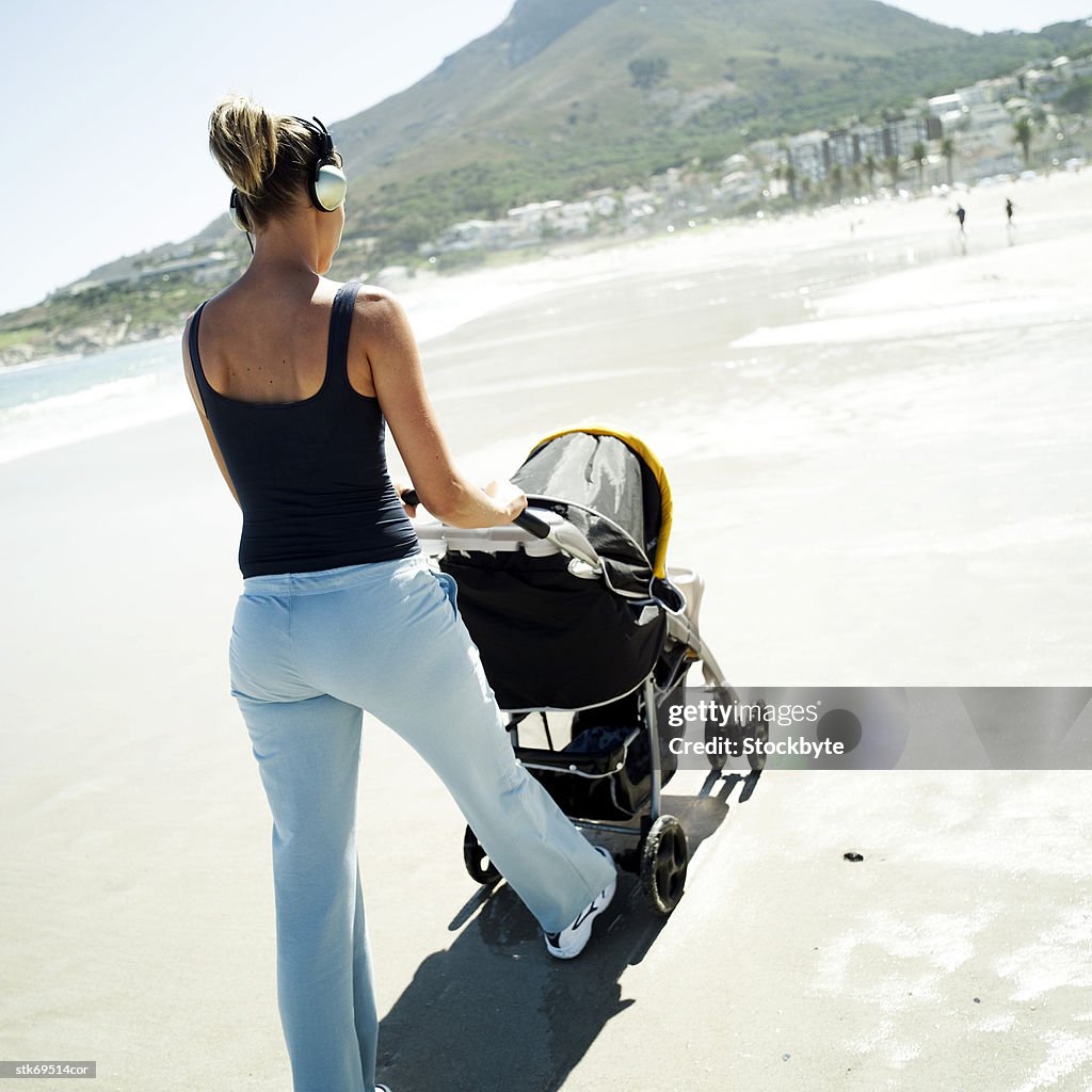View from behind of a woman walking her baby in a stroller on the beach