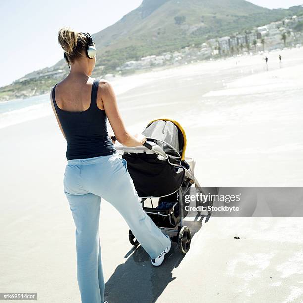 view from behind of a woman walking her baby in a stroller on the beach - audio hardware stock pictures, royalty-free photos & images