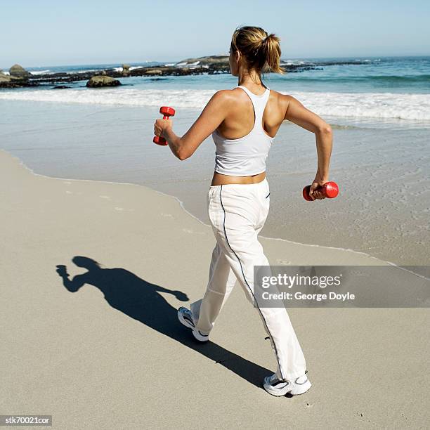 rear view of a woman walking on the beach with dumbbells - anaerob träning bildbanksfoton och bilder