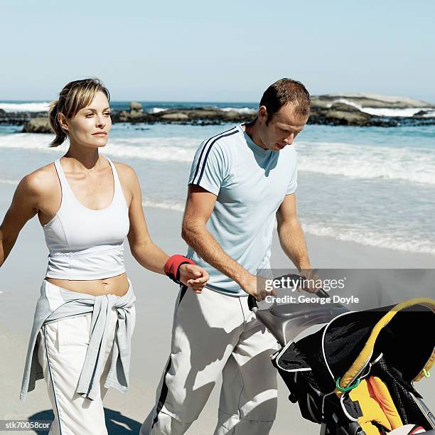 couple walking on the beach with a stroller - human powered vehicle stock pictures, royalty-free photos & images