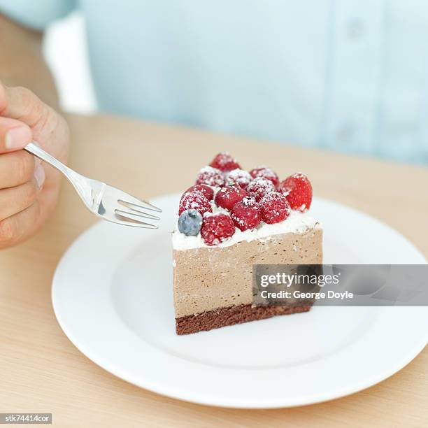 close-up of a man's hand holding a fork beside a slice of mousse cake - slice stock pictures, royalty-free photos & images