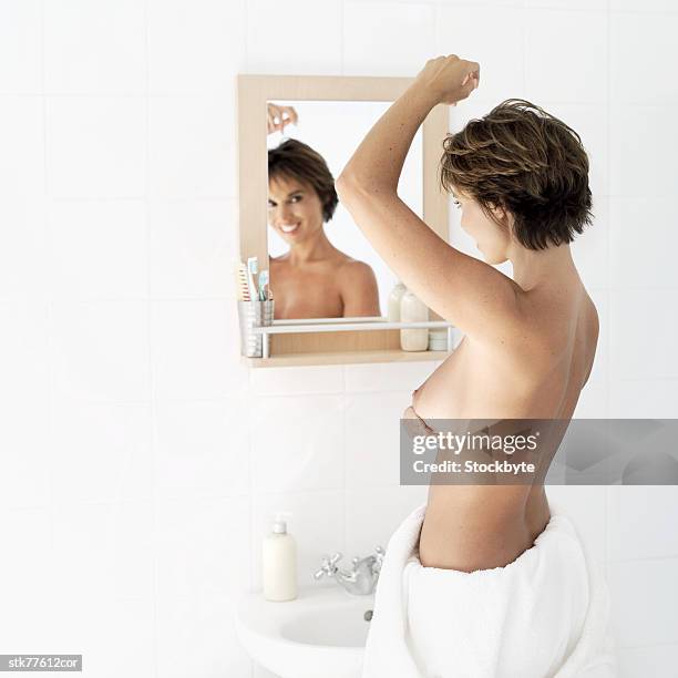 side profile of a nude woman looking in a mirror and touching her breast - alleen mid volwassen vrouwen stockfoto's en -beelden