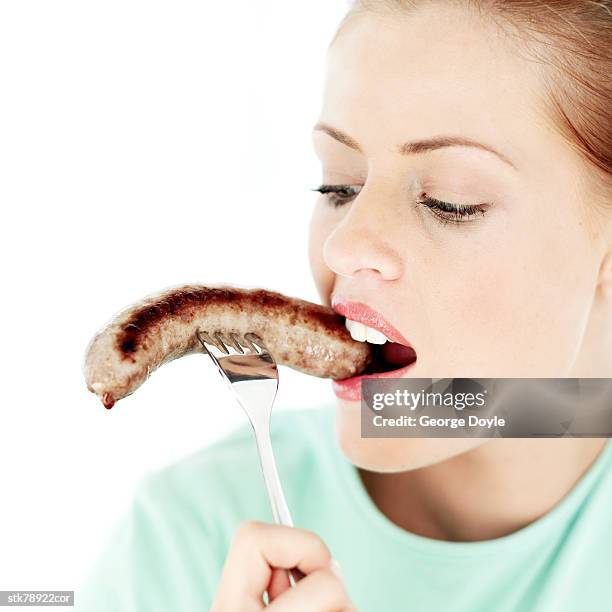 portrait of a young woman biting a sausage on a fork - forma de falo fotografías e imágenes de stock