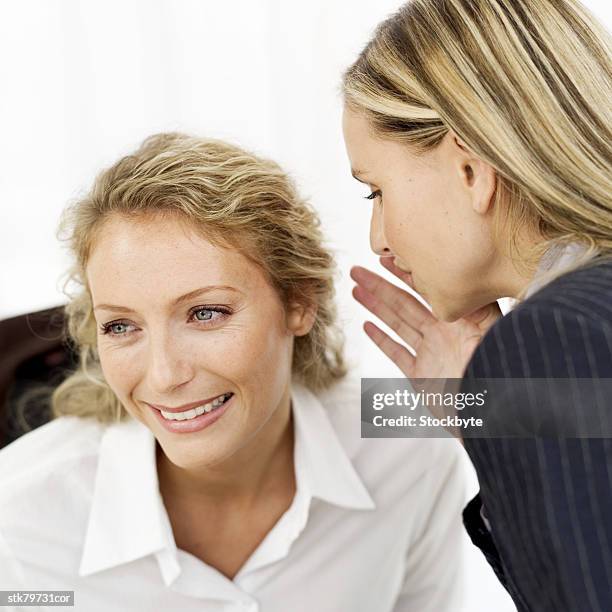 a businesswoman whispering into a woman's ear - alleen mid volwassen vrouwen stockfoto's en -beelden