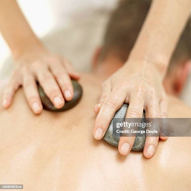 woman massaging a man's back with therapeutic massage stones - dos humain photos et images de collection