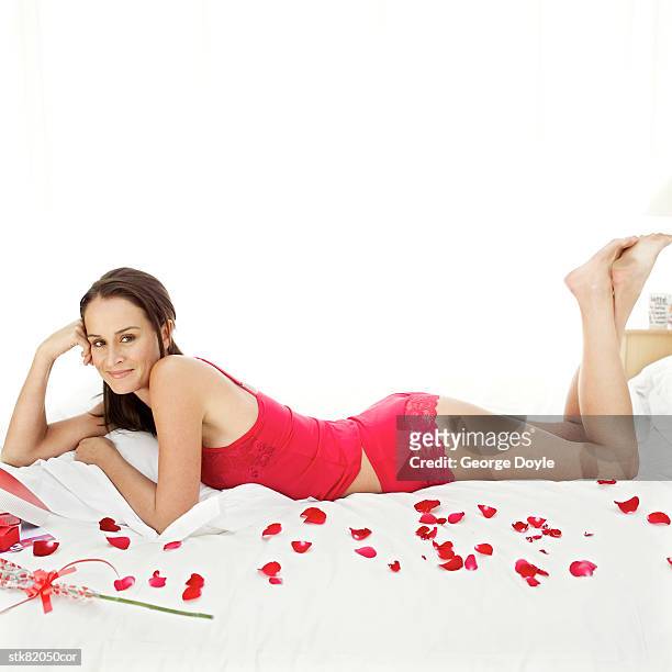 portrait of a young woman lying on bed covered with rose petals - hinge joint stock pictures, royalty-free photos & images