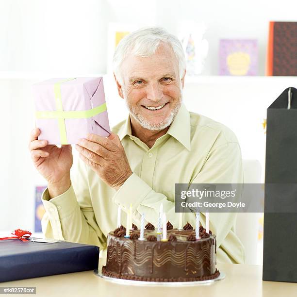 portrait of an elderly man holding up a present for a birthday celebration - house and senate dems outline constitutional case for trump to obtain congressional consent before accepting foreign payments or gifts fotografías e imágenes de stock