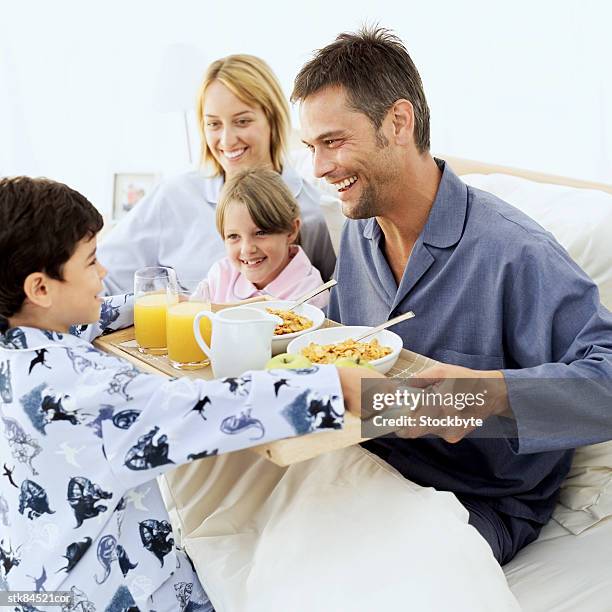 side profile of a boy handing his parents and sister breakfast in bed - side by side photos et images de collection